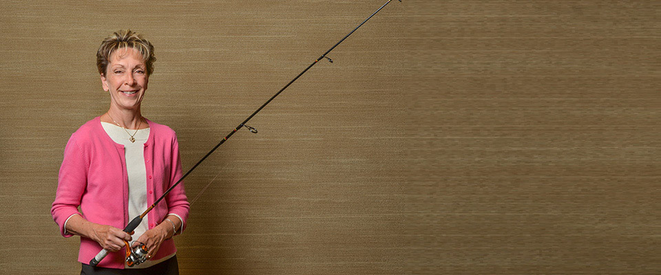 Don Hannah wearing a white polo shirt, standing in front of a gold backdrop and holding a fishing pole.